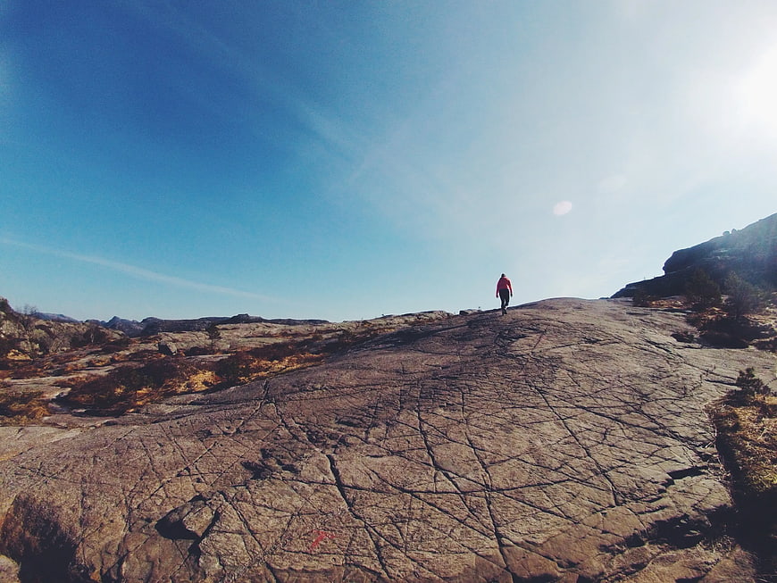 Hiker walking on vast granite rock formation under blue sky