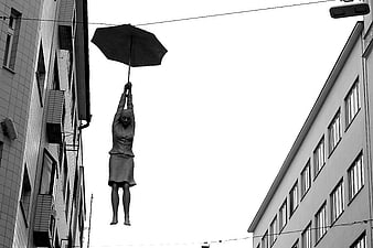 Black and white sculpture of woman hanging from umbrella in urban street