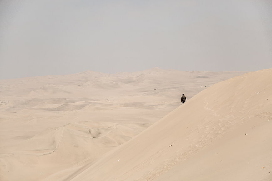 Lone figure walking on vast sand dunes in desert landscape