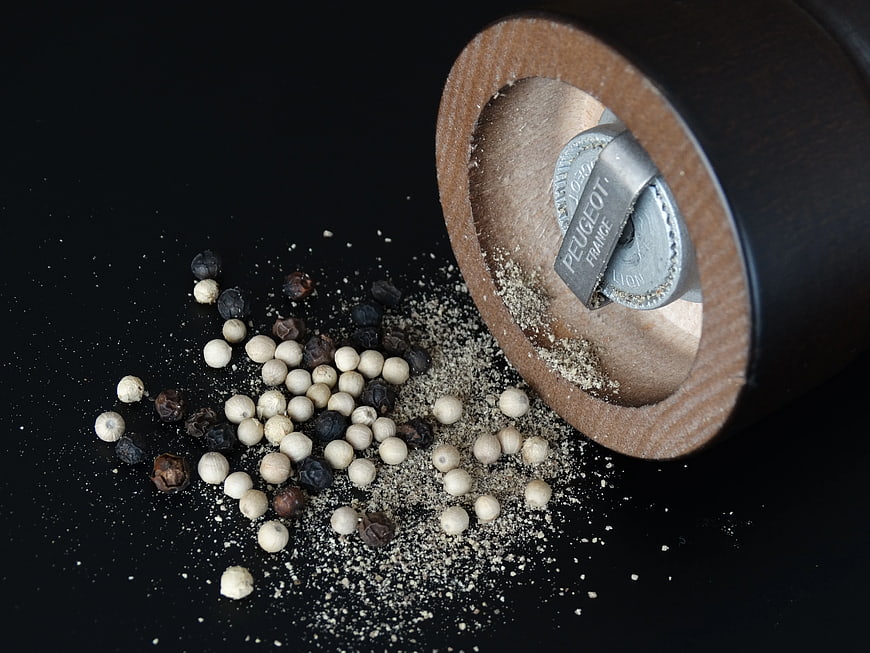 Wooden Pepper Mill with Spilled White and Black Peppercorns