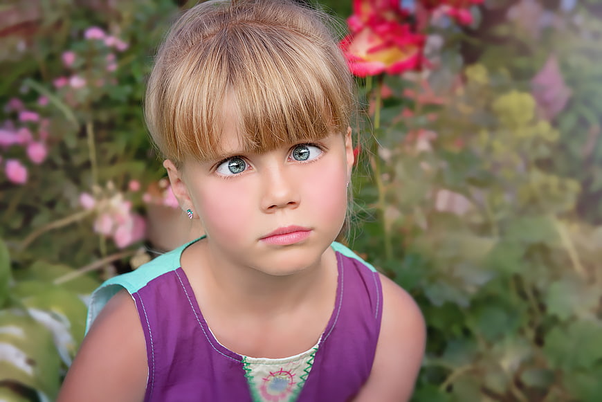 Portrait of a young blonde girl with blue eyes in a garden