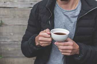 Man holding white cup of tea in black jacket