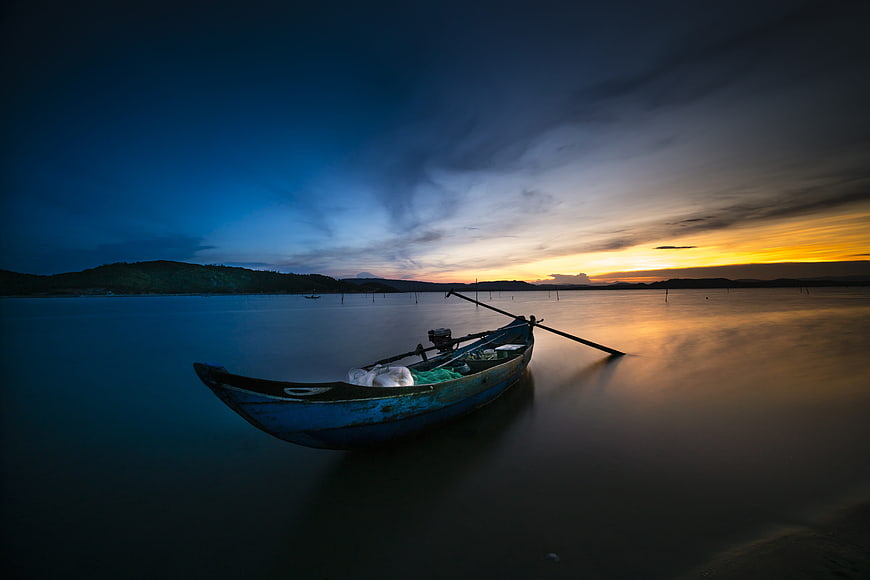 Solitary blue fishing boat on calm water at sunset
