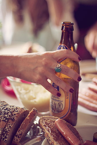 Woman's hand holding beer bottle with bread and sausage