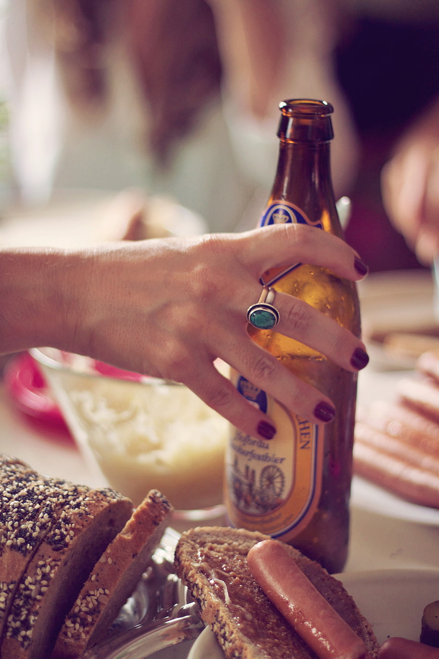 Woman's hand holding beer bottle with bread and sausage