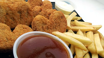 Close-up of breaded chicken nuggets, french fries, and dipping sauces