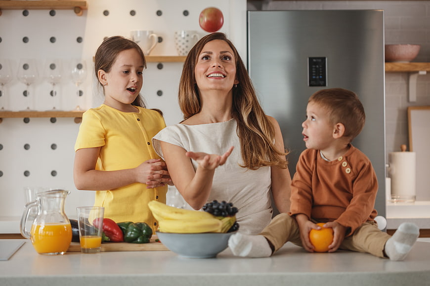 Happy mother and children playing with fruit in kitchen
