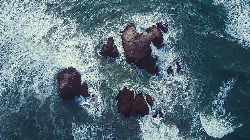 Aerial View of Ocean Waves Crashing on Dark Rocks