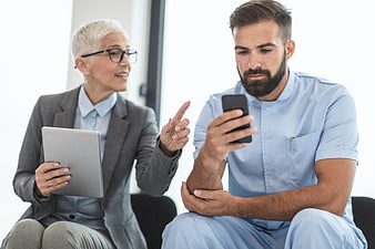 Senior female doctor consulting with male nurse holding smartphone