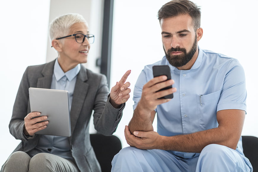 Senior female doctor consulting with male nurse holding smartphone