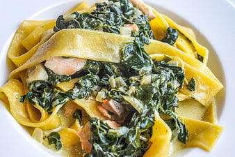 Close-up of fresh tagliatelle pasta with spinach and mushrooms in a white bowl