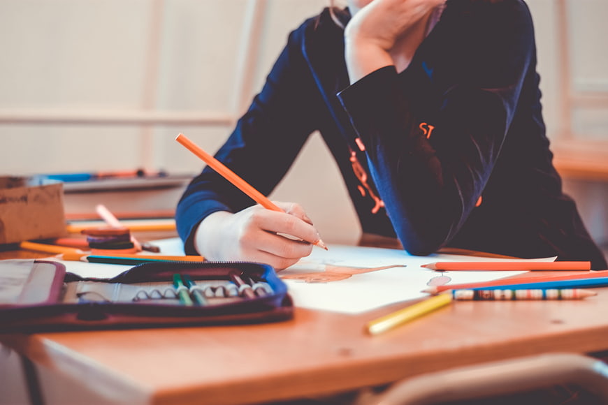 Student Drawing With Colored Pencils In Classroom