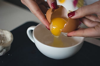 Close-up of hands cracking a fresh egg into a white bowl