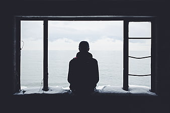 Silhouette of Man Looking Out Window at Ocean in Winter