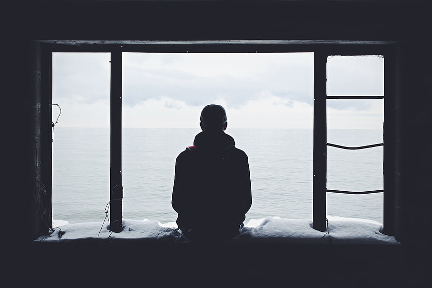 Silhouette of Man Looking Out Window at Ocean in Winter