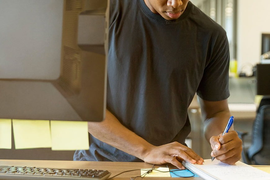 Man Writing Notes at Office Desk with Computer
