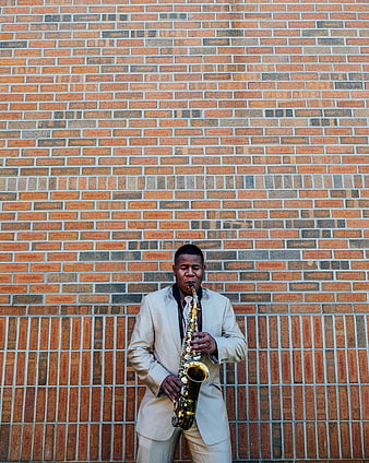 Man in beige suit playing saxophone against brick wall