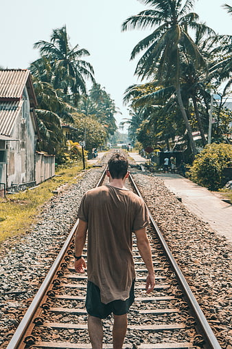Man Walking Away on Train Tracks in Tropical Village