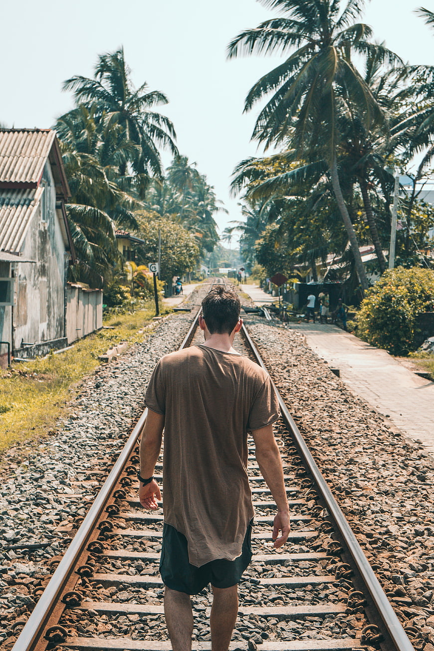 Man Walking Away on Train Tracks in Tropical Village