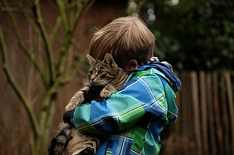 Young boy hugging a tabby cat outdoors in a blue plaid jacket