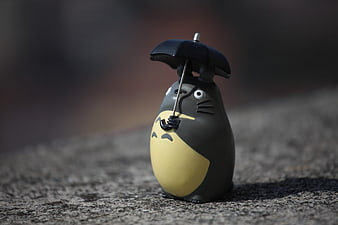 Totoro toy figure holding a black umbrella on a textured stone surface