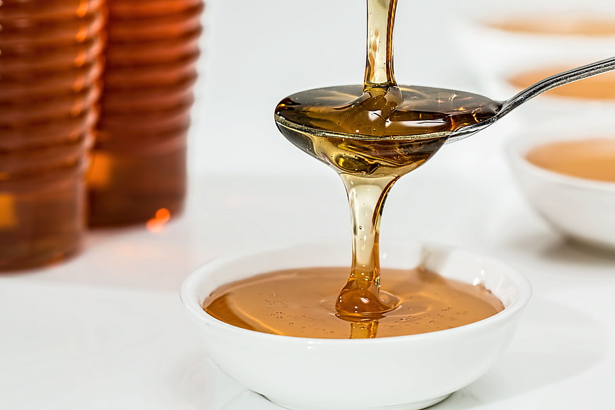 Golden Honey Pouring from Spoon into White Bowl
