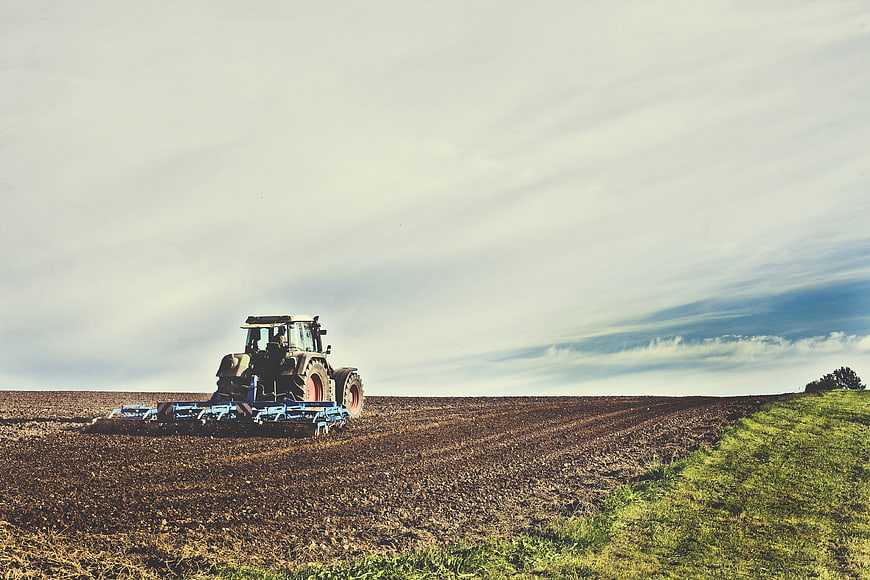 Tractor tilling a field under a cloudy sky