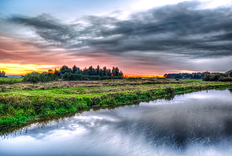 Dramatic Sunset Over River and Green Fields