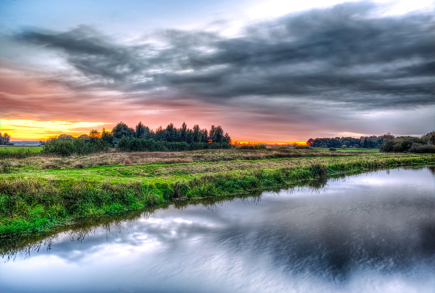Dramatic Sunset Over River and Green Fields