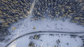 Aerial view of cars driving on snowy winter forest road