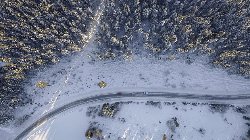 Aerial view of cars driving on snowy winter forest road