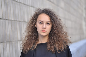 Portrait of young woman with curly hair against concrete wall