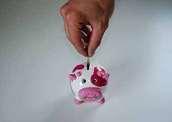 Hand inserting coin into pink and white piggy bank