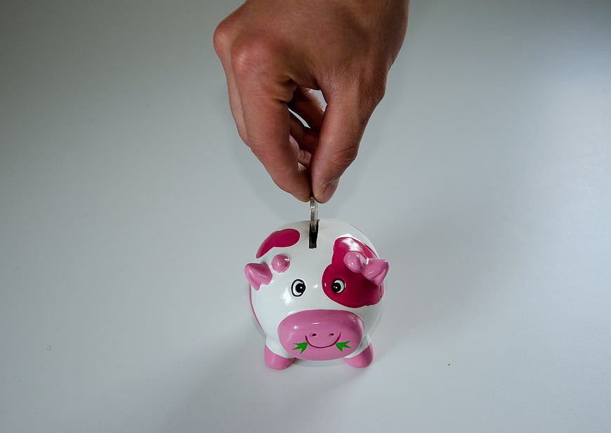 Hand inserting coin into pink and white piggy bank
