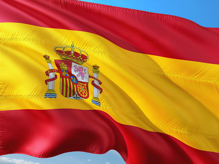 Waving Spanish Flag with Coat of Arms Against Blue Sky