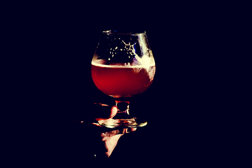 Hand holding amber beer glass against dark background