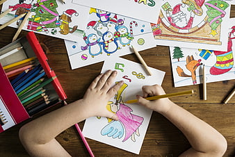 Child coloring Christmas pictures with colored pencils on wooden table