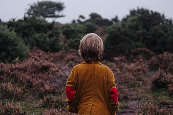 Child in mustard jacket exploring moody heathland landscape