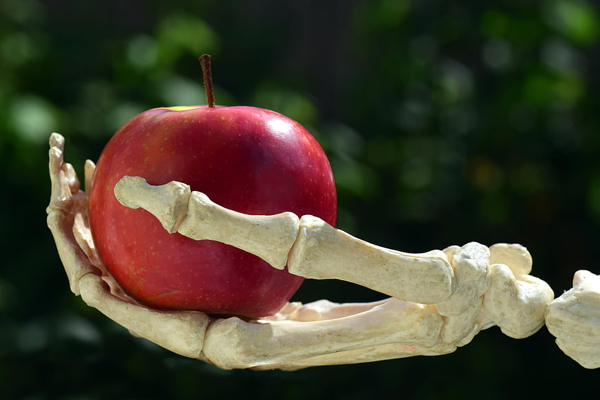 Skeletal hand holding a red apple against a blurred green background