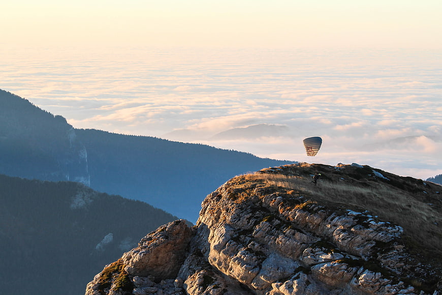 Paraglider launching from mountain peak above sea of clouds