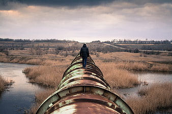 Man Walking on Large Rusty Pipeline Over River