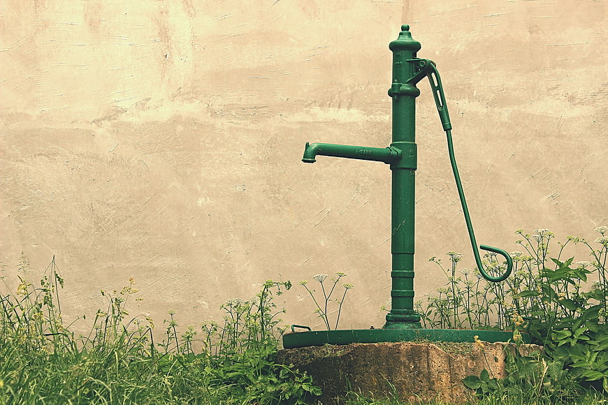 Vintage green manual water pump against beige wall