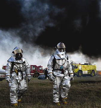 Firefighters in silver proximity suits walking near emergency vehicles