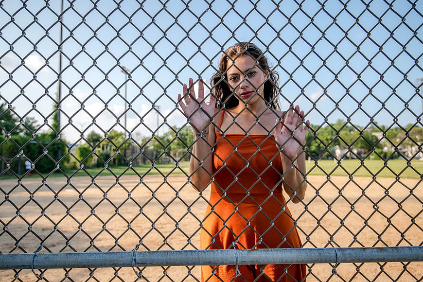 Woman in Orange Dress Behind Chain Link Fence