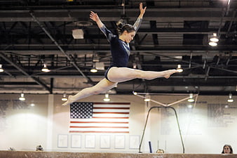 Female gymnast performing a split leap on the balance beam