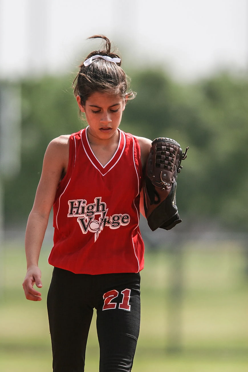 Young female softball player in red uniform walking on field
