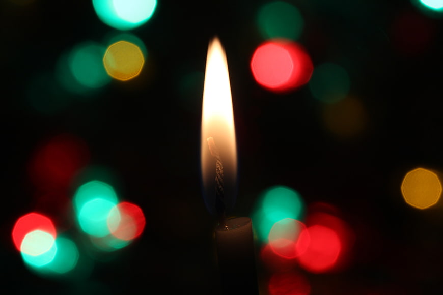 Single lit candle flame with colorful bokeh background