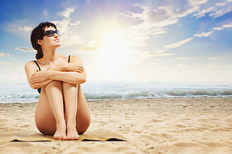 Woman in bikini sitting on beach towel with sun flare