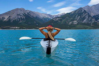 Woman kayaking on turquoise lake with mountains