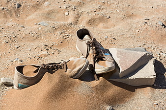 Old worn sneakers half buried in desert sand